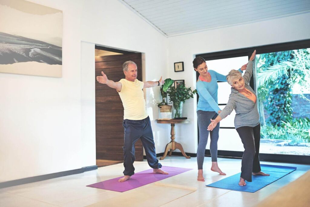 Yoga instructor guiding a senior couple in a yoga class