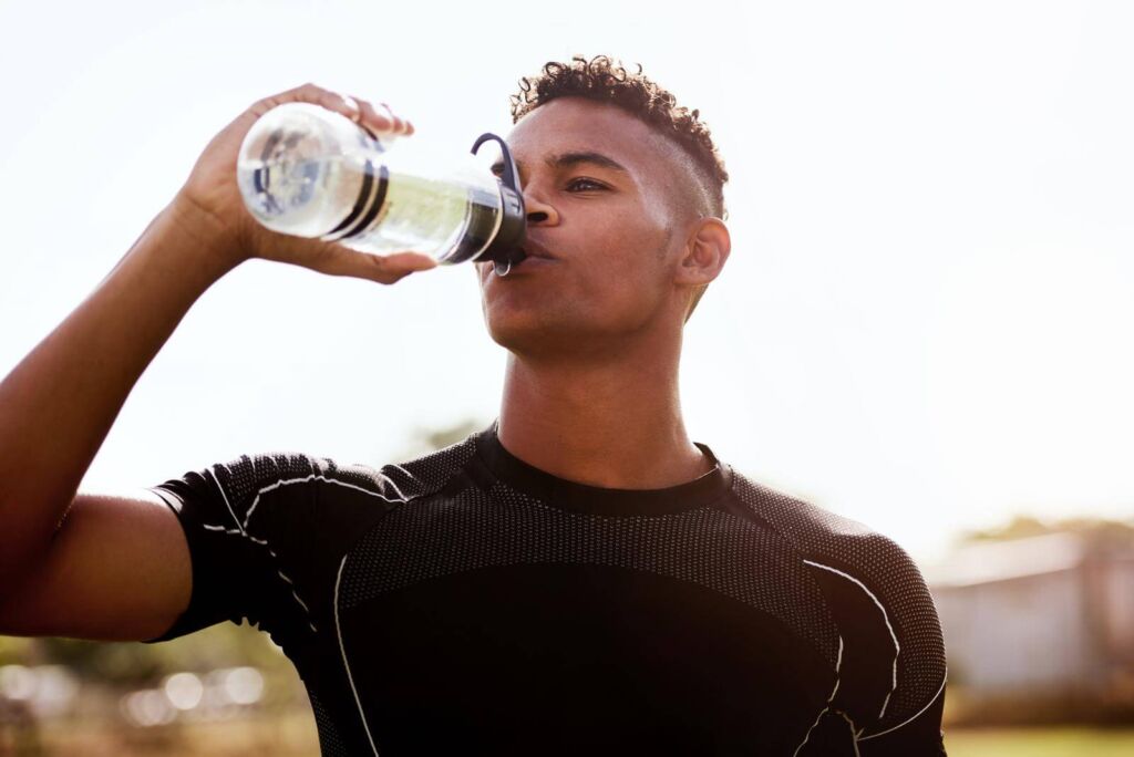 Young man drinking water after playing a game of rugby.