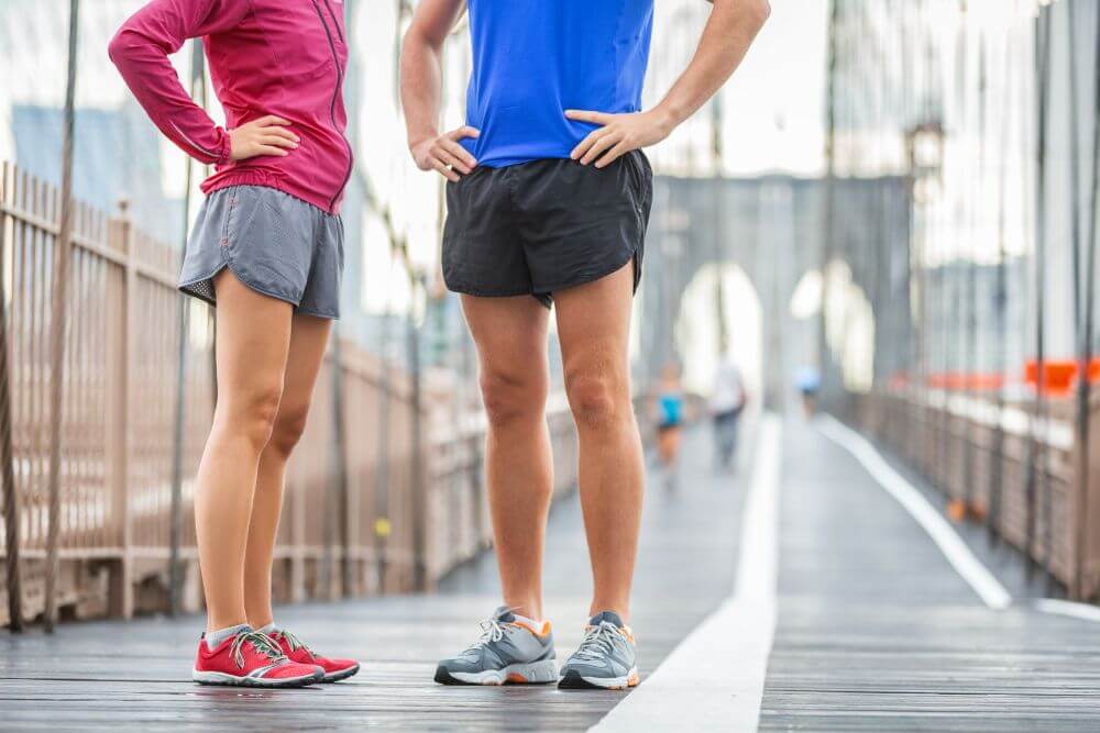 Runners legs training on Brooklyn bridge talking together before morning training run wearing run shorts and running shoes.